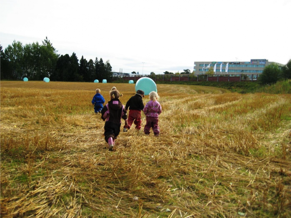 Barn løper på en eng med høyballer.