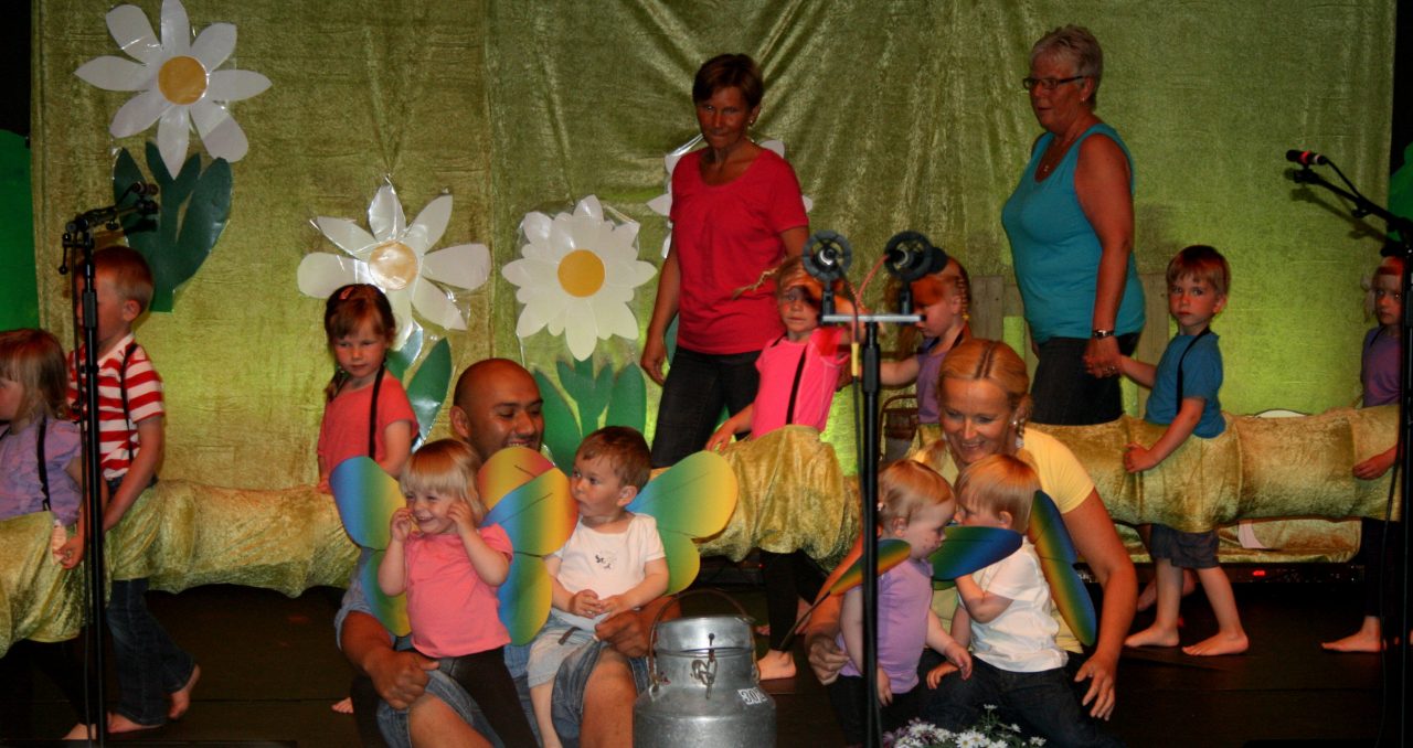 Barn og voksne på scenen i fargeriker klær.