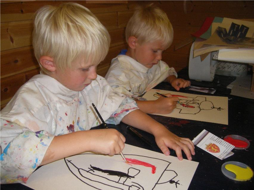 To gutter sitter ved et bord og maler.