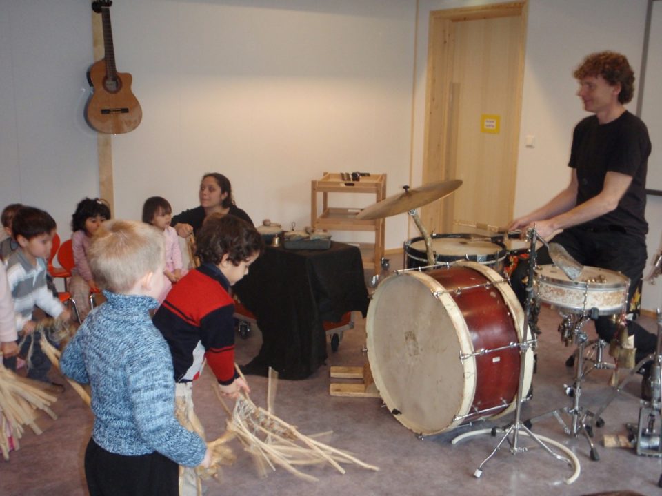 Barn eksperimenterer med instrumenter, voksen spiller trommer.