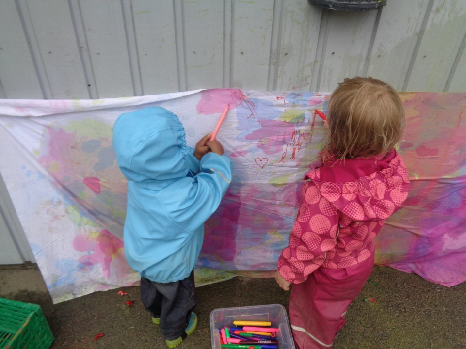 Barn maler på et lerret som henger på en vegg ute.