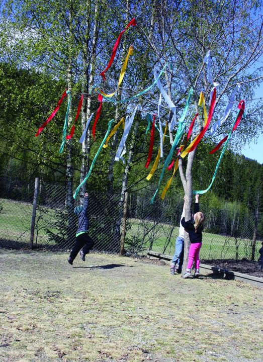 Barn står ved et tre som har fargerike strimler festet på greinene.