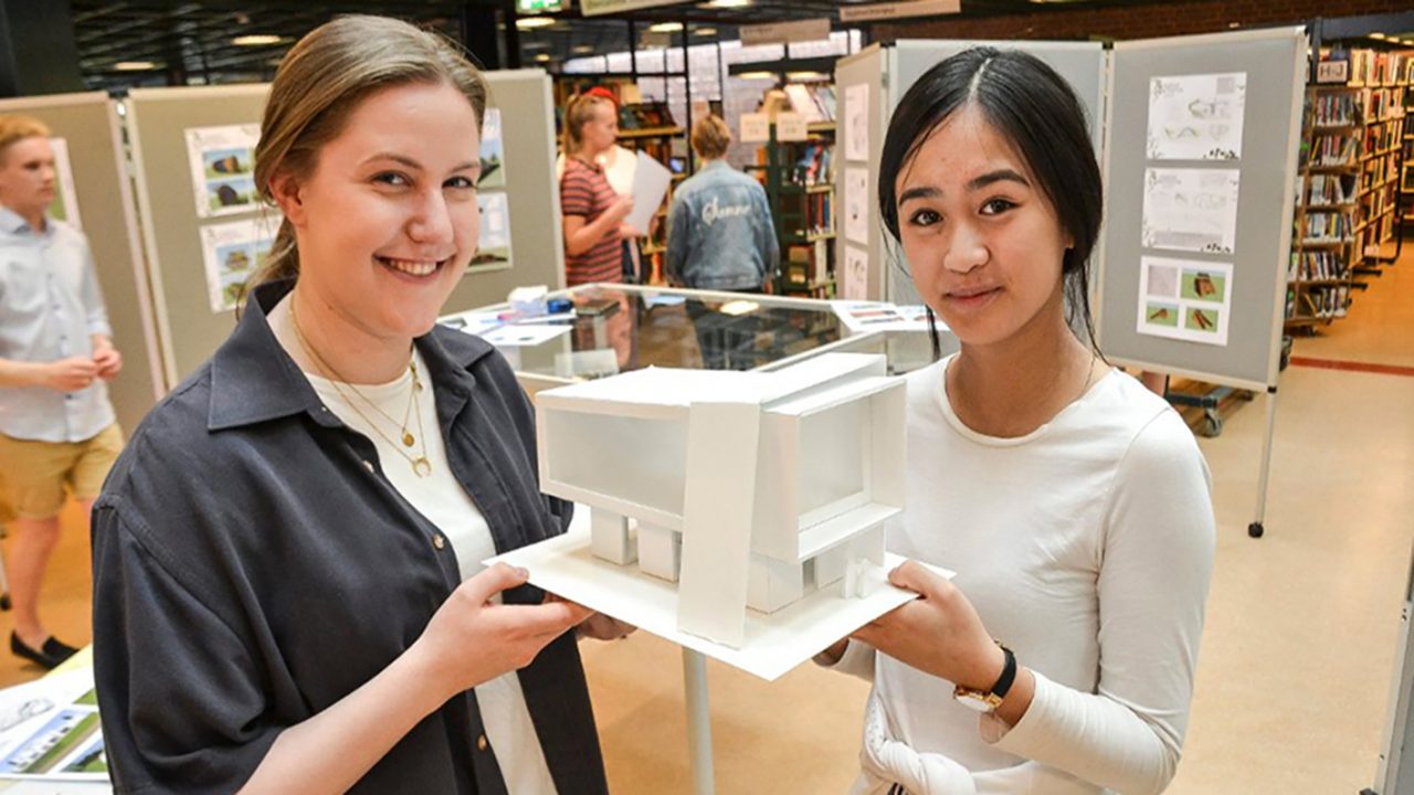 To elever holder opp en arkitekturmodell laget av kapapapp.