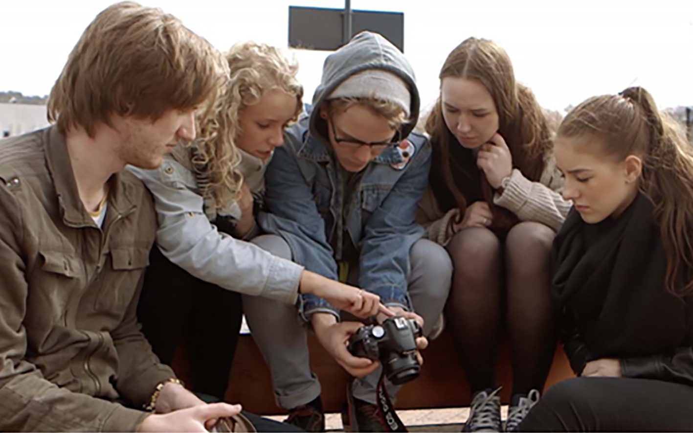 Ungdommer kommuniserer med hverandre rundt et fotoapparat. Detalj av hender som arbeider på PC med bilderedigering