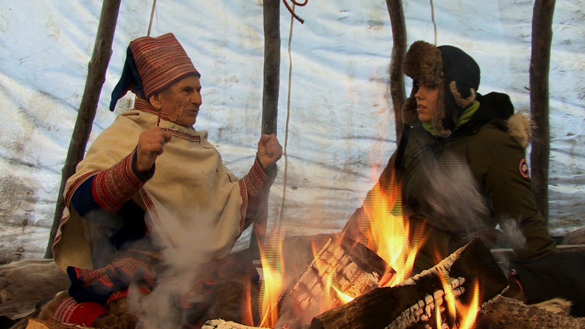 Gammel samisk mann i samtale med ung kvinne bak bålet