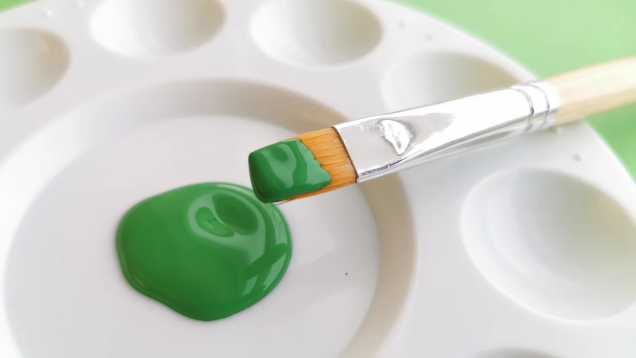 Hvit palett med grønn maling, pensel med grønn maling og grønn bakgrunn