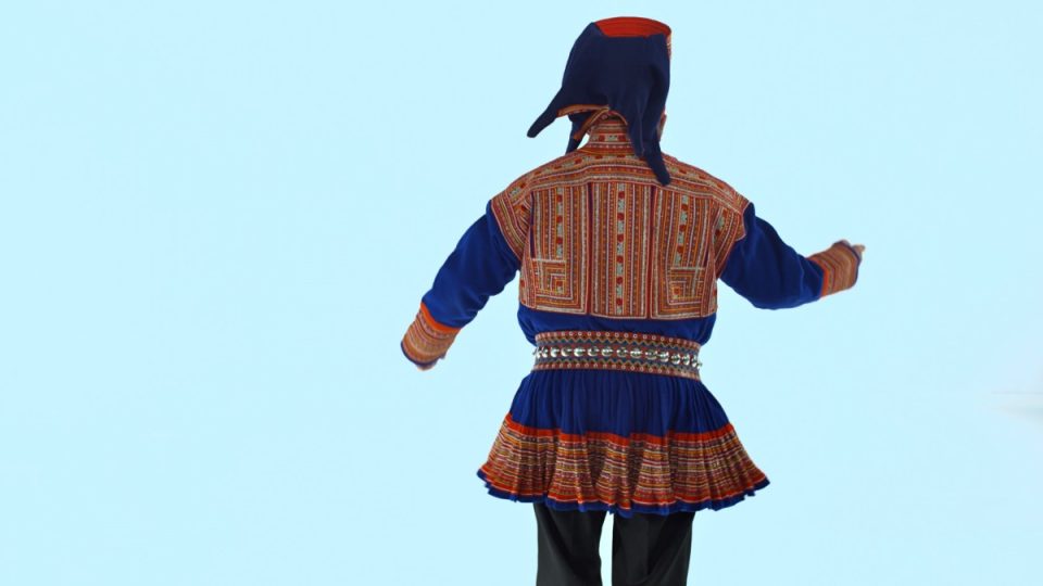 Mann i samisk kofte står med ryggen til. Holder høyre nånd foran seg. 