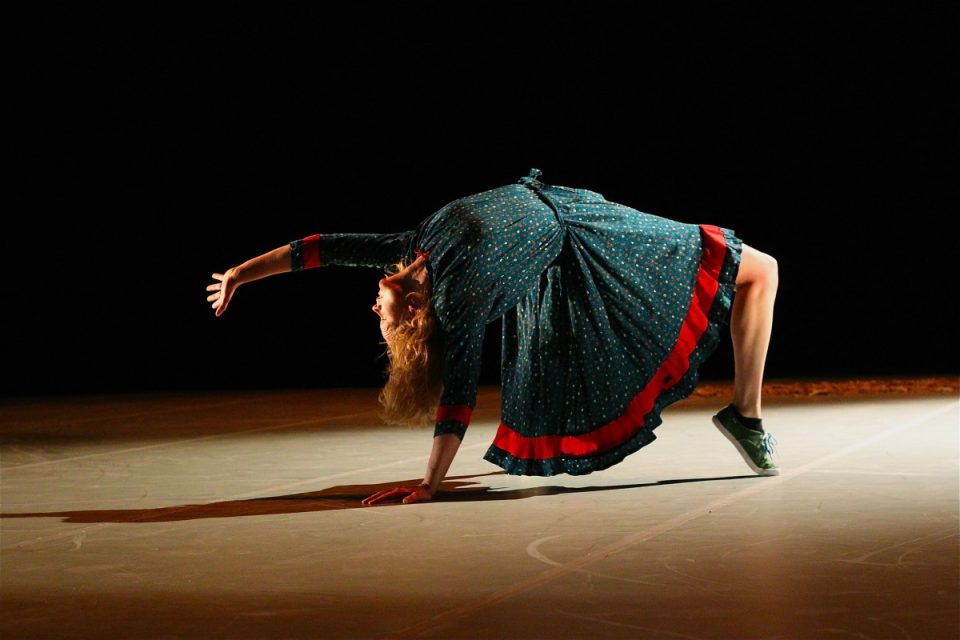 Kvinne med blå og rød samisk kofte står i bru på gulvet.