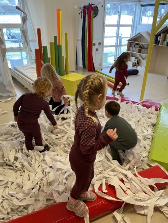 Barn leker i et mylder av hvite papirstrimler.