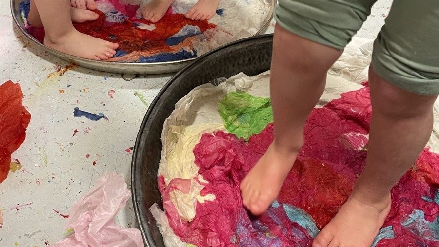 Barn som trår barbeint på fargerikt papir. 