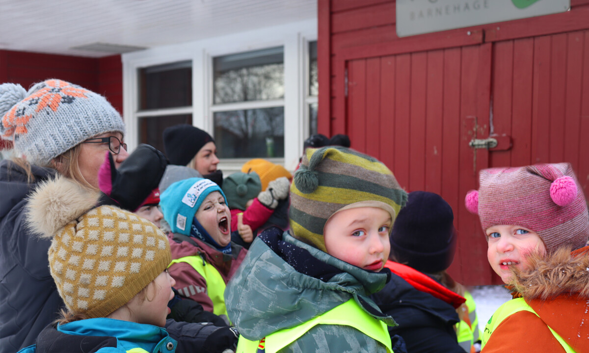 En gruppe med barn sitter samlet ute og synger ikledd vinterklær.