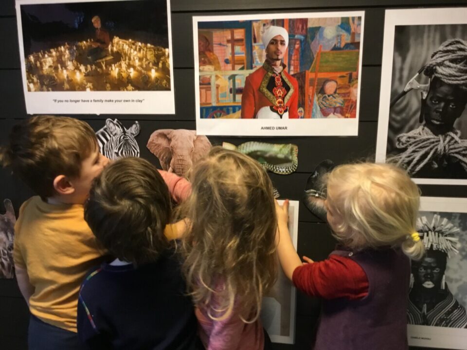Barn står foran en vegg av foto av ulike kunstnere. 