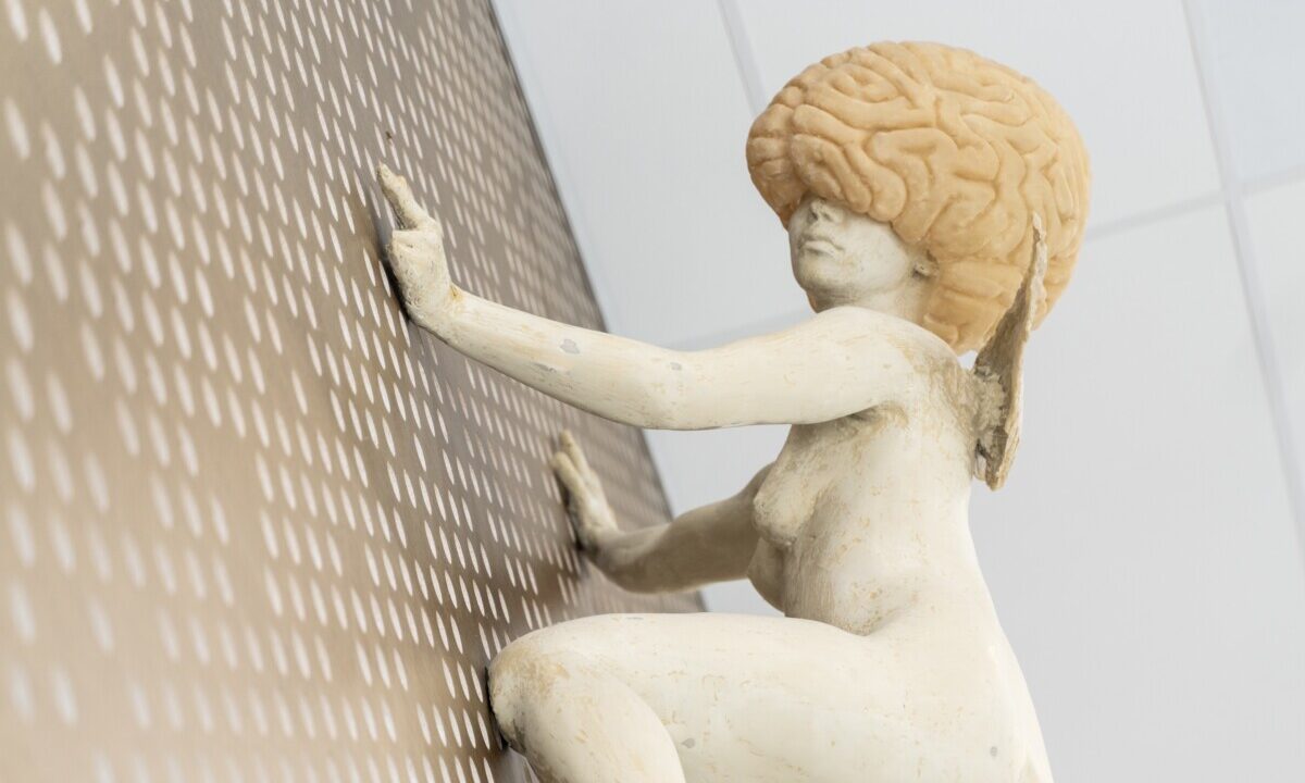 Kunstverk. Hvit dame som klatrer på en vegg. Hodet er formet som en hjerne